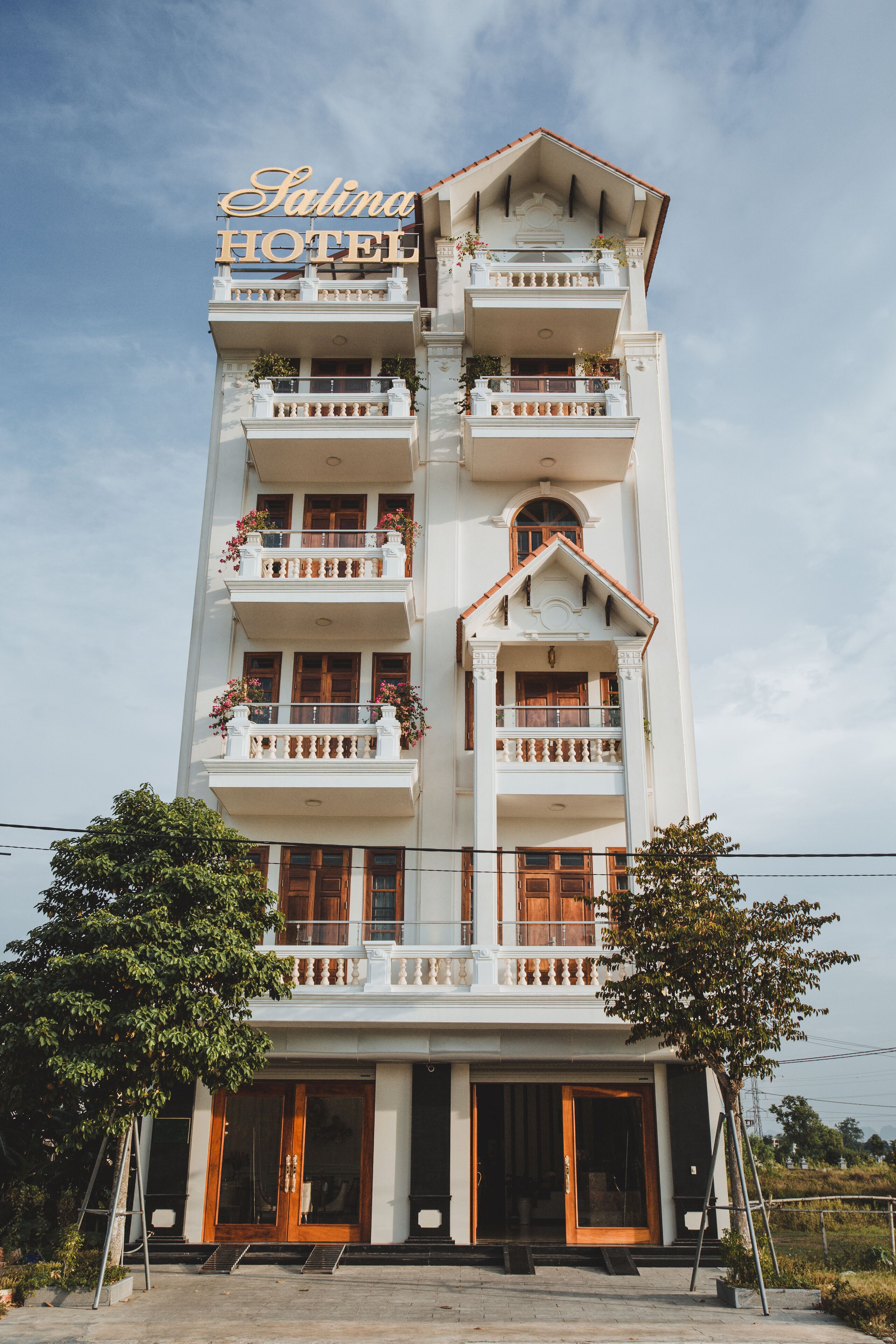 A multi-story hotel with a prominent sign reading "Sarina Hotel". The building features balconies with railings and potted plants.