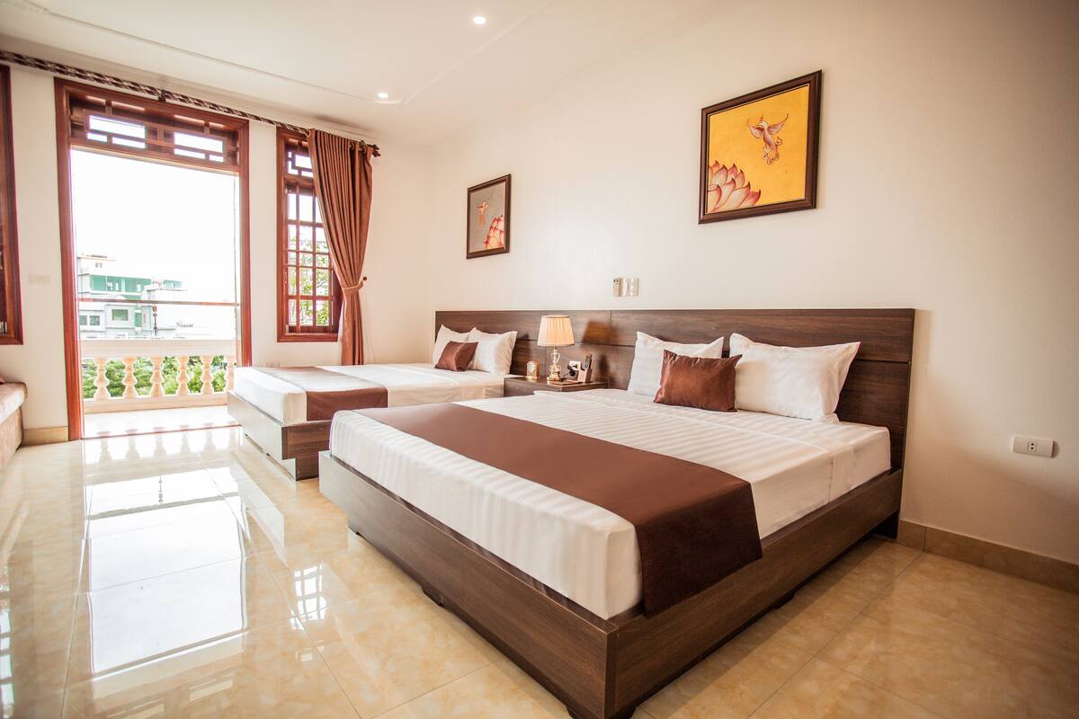 A hotel room with a large bed, a smaller bed, a balcony with a view, and a painting on the wall.