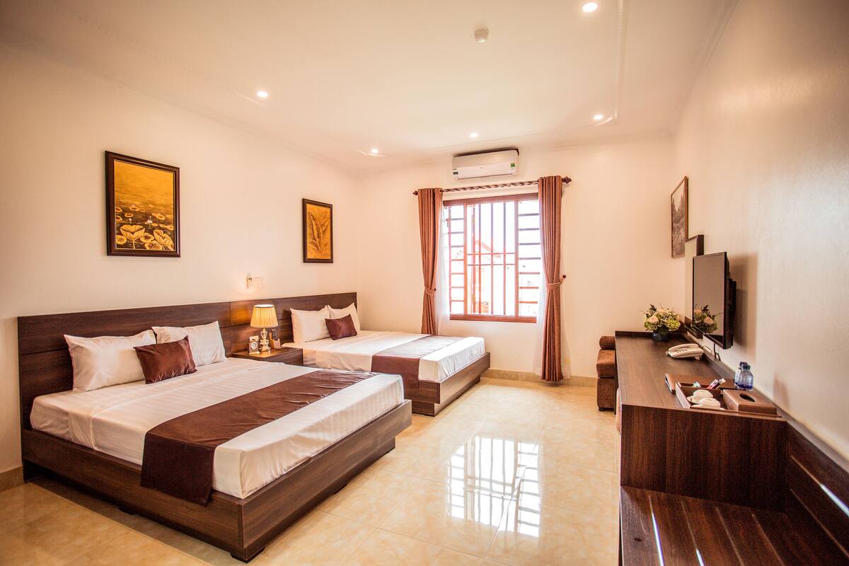 A hotel room with two beds, a desk, a TV, and artwork on the walls.