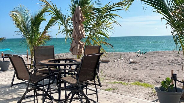 Eine Terrasse mit Tisch und Stühlen, einem Sonnenschirm und Blick auf Strand und Meer.