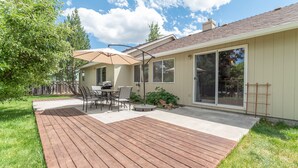 A patio with a wooden deck, a table with chairs, and a large umbrella. - Furnished 30+ day rental close to Old Mill! Dog Friendly! (Bend)