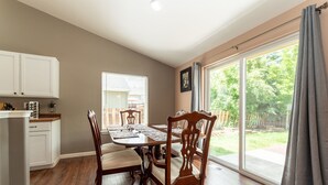 A dining area with a wooden table and chairs, a kitchen with white cabinets, and a large sliding glass door leading to a backyard. - Furnished 30+ day rental close to Old Mill! Dog Friendly! (Bend)
