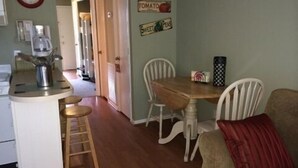 A kitchen with a wooden table and white chairs, a coffee maker, and a clock on the wall.