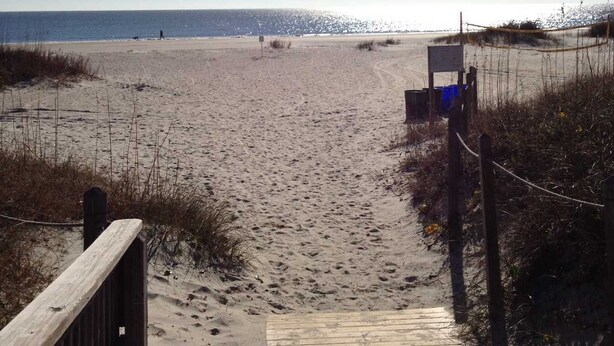 A wooden boardwalk leading to a beach with a clear sky.