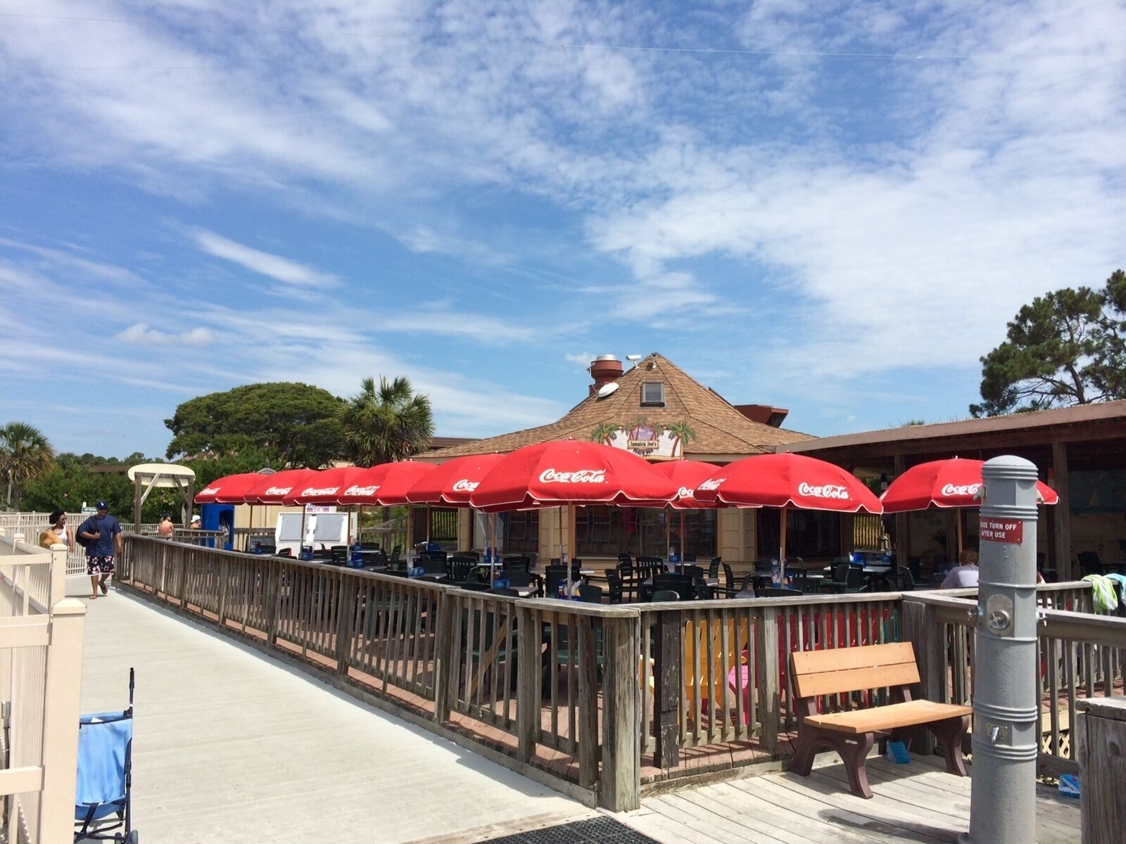 A boardwalk with red umbrellas, a wooden fence, and a building with a sign.