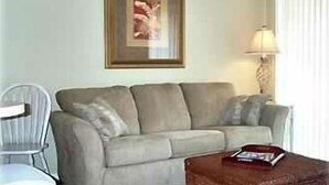 A living room with a sofa, a chair, a lamp, and a framed picture on the wall.
