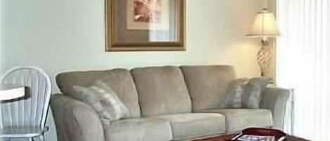 A living room with a sofa, a chair, a lamp, and a framed picture on the wall.