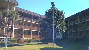 A multi-story hotel with balconies, a parking lot, and a grassy area with trees.