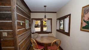 Une salle à manger en bois avec une table ronde et des chaises, un luminaire suspendu et une fenêtre avec des rideaux.