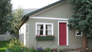 Une maison de plain-pied avec une porte rouge, des fenêtres à cadre blanc et une petite jardinière à l’avant.