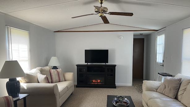 Un salon doté d’un ventilateur de plafond, d’une cheminée, d’un téléviseur et de deux canapés.