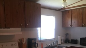 Une cuisine de taille réduite, avec des meubles de rangement en bois, une cuisinière, un évier et une fenêtre.