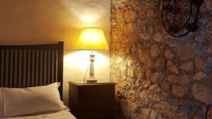 Ein Bett mit zwei aufgerollten Handtüchern, ein Nachttisch mit Lampe und eine Steinwand.