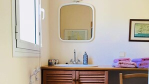 Ein Badezimmer mit einem Holzkosmetikschrank, einem Waschbecken, einem Spiegel und einem Stuhl.