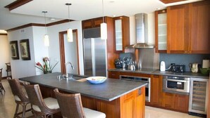Una cocina moderna con una isla central, armarios de madera, electrodomésticos de acero inoxidable y sillas de mimbre.