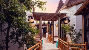 A wooden pathway leading to a covered area with hanging lanterns, surrounded by greenery and stone walls.