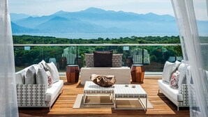 A balcony with a view of mountains and a body of water, furnished with a sofa, a table, and decorative items.