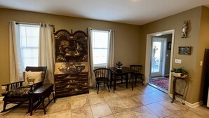 A dining area with a wooden bench, a table, and chairs. There is a decorative wall panel and a small plant on a stand.