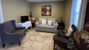 A living room with a grey sofa, a blue armchair, a TV on a table, and a painting on the wall.