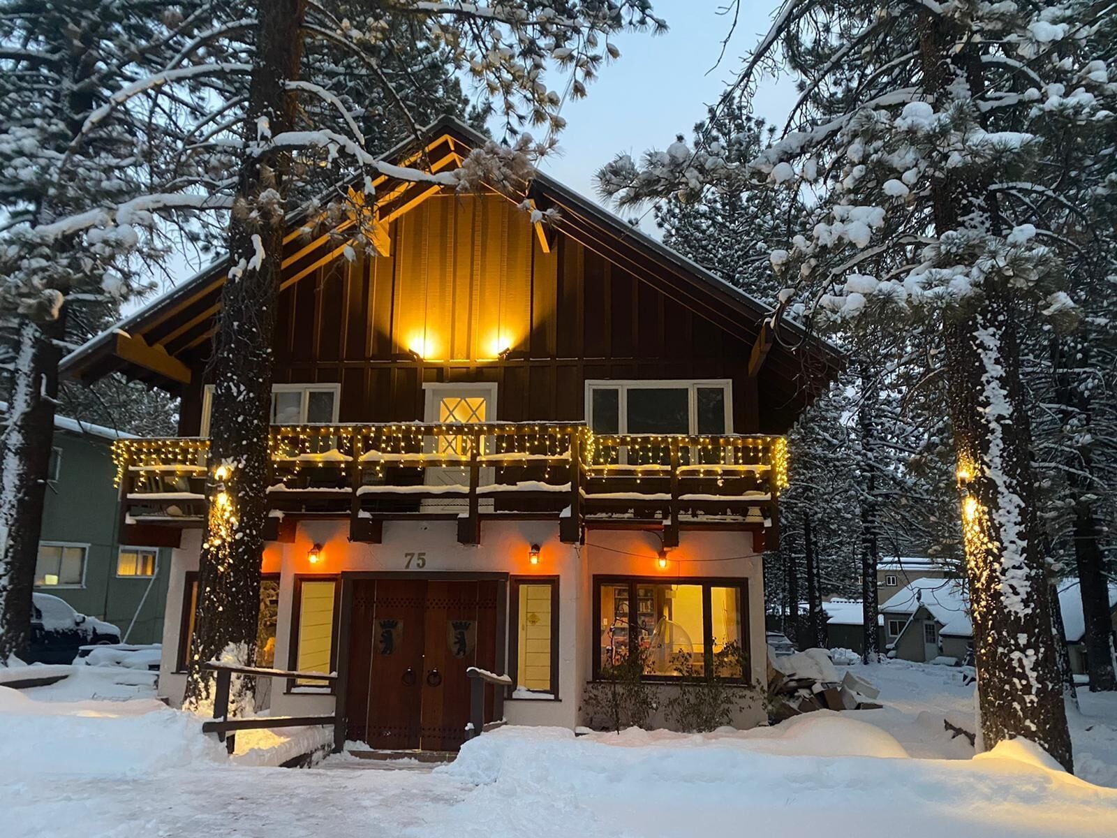 A two-story lodge with a balcony, snow-covered trees, and a warm-lit entrance.