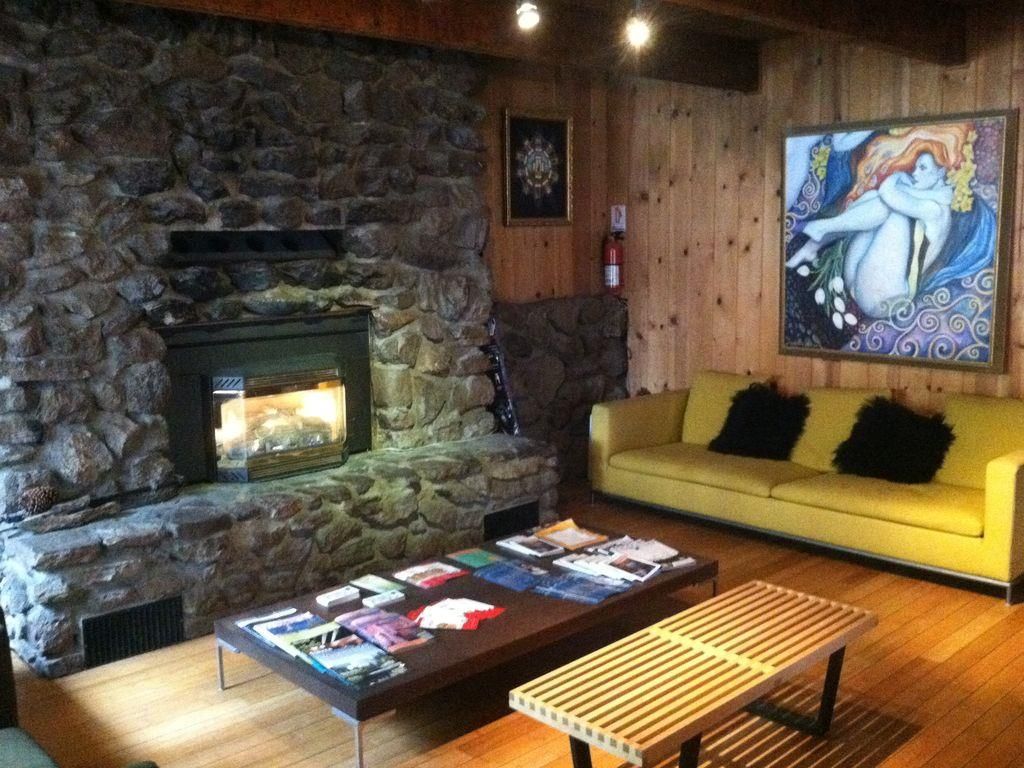 A stone fireplace, a yellow sofa, and a wooden coffee table with magazines.