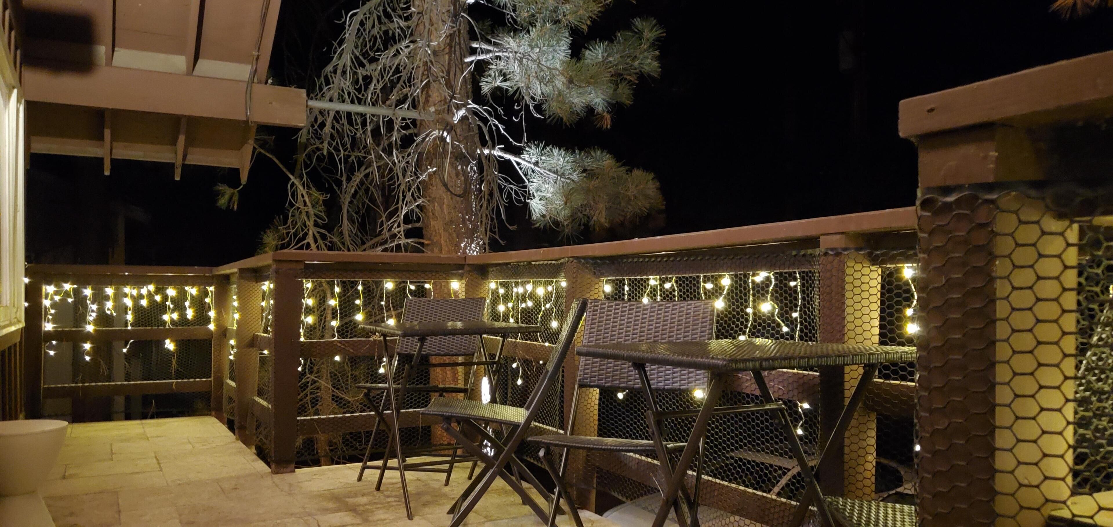 An outdoor patio area with metal chairs and tables, decorated with string lights.