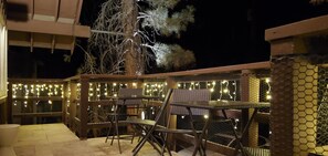 Ein Terrassenbereich im Freien mit Metallstühlen und -tischen, geschmückt mit Lichterketten.