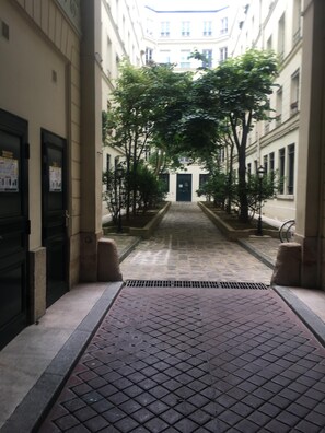 Un pasillo estrecho con suelo de baldosas, flanqueado por edificios con grandes ventanas y puertas.