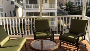 Un balcon doté de fauteuils en osier et d’une table en verre, offrant une vue sur un quartier résidentiel avec des immeubles à plusieurs étages.