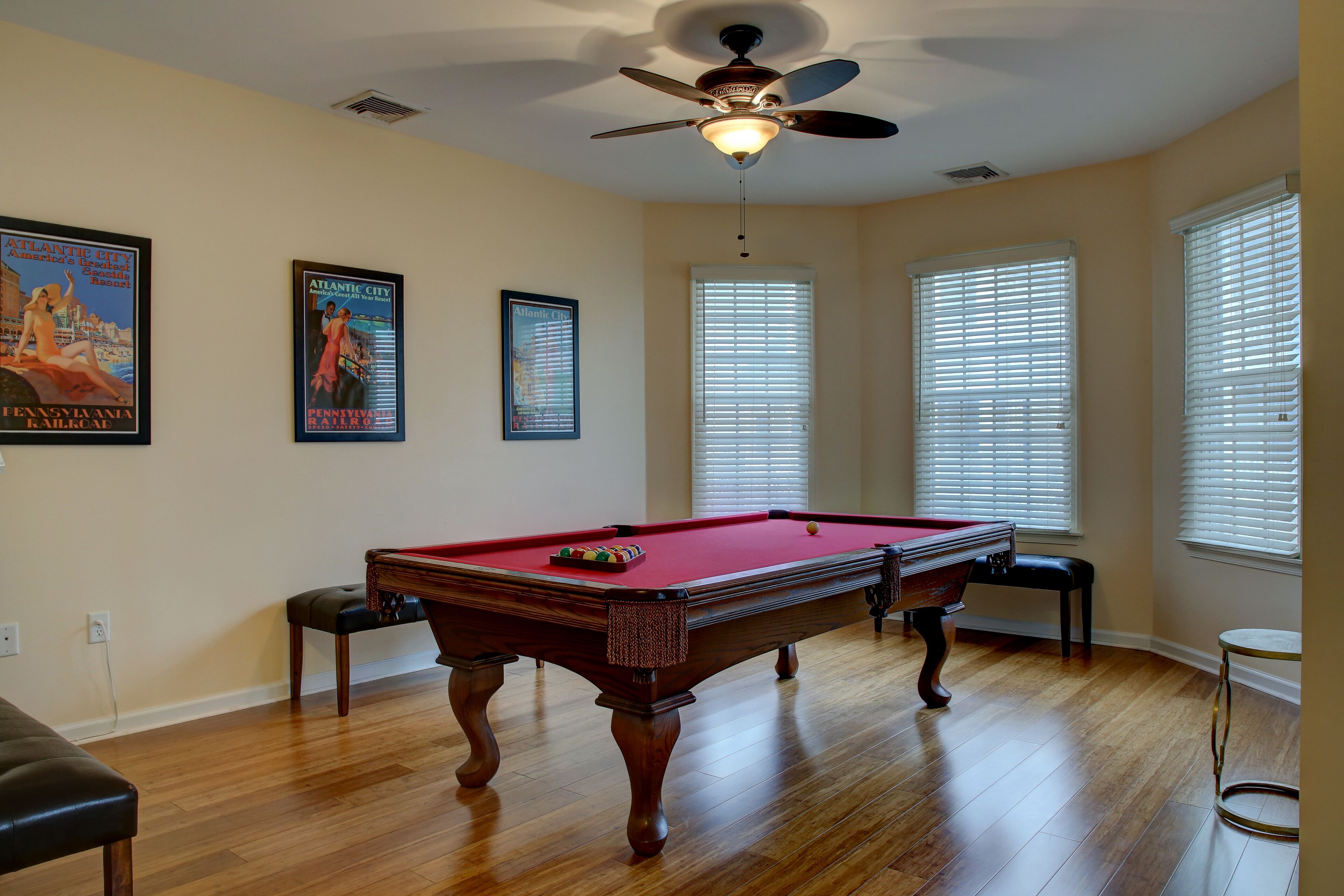 A pool table with a ceiling fan, wooden flooring, and two framed posters on the wall.