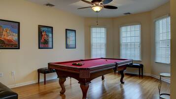 A pool table with a ceiling fan, wooden flooring, and two framed posters on the wall.