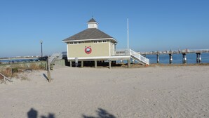 Un poste de surveillance de plage avec une tour de surveillance, une jetée s’avançant dans l’eau et un ciel bleu dégagé.