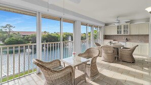 A balcony with wicker furniture overlooking a body of water, a kitchen area with white cabinets, and a ceiling fan. - Resort Living @ Its Finest!  Spacious 2 Bed 2 Bath Condo! (Naples)