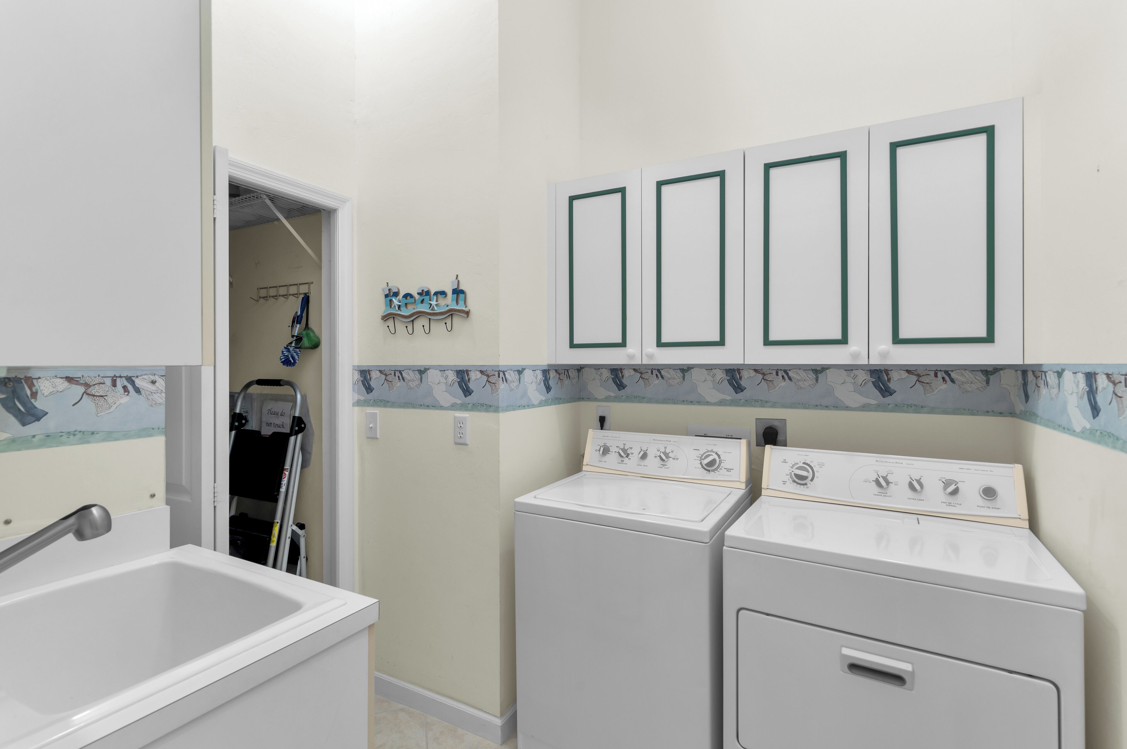 Un lavadero con dos lavadoras y secadoras apiladas, un lavamanos y una puerta que da a otra habitación.