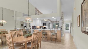A spacious kitchen with a central island, wooden dining table with chairs, and hanging pendant lights. - Resort Living @ Its Finest!  Spacious 2 Bed 2 Bath Condo! (Naples)