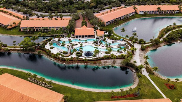 An aerial view of a resort with multiple swimming pools, a central water feature, and surrounding greenery. - Resort Living @ Its Finest!  Spacious 2 Bed 2 Bath Condo! (Naples)