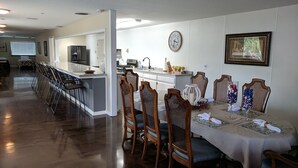 Un comedor espacioso con una larga mesa, sillas de madera y una cocina al fondo.