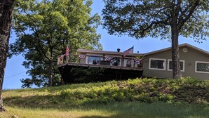 Una casa con un porche, una bandera estadounidense y un gran árbol al fondo.