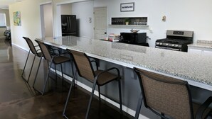 Una cocina con encimera de granito, cuatro taburetes de bar, un refrigerador, un microondas y una estufa.
