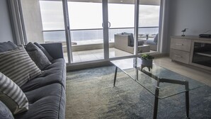 A modern living room with a sofa, a glass coffee table, and a view of the ocean through large sliding doors. - Oceanfront Brand New Unit at La Jolla Excellence
The Pelican  (Playa Encantada)