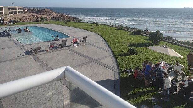 A pool area with a view of the ocean, lounge chairs, and a grassy area with people. - Oceanfront Brand New Unit at La Jolla Excellence
The Pelican  (Playa Encantada)