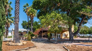 A building with a covered patio area, surrounded by trees and a dirt path. - Sleeps 10 + Spa + Foosball | 3 Acres of Rural Privacy | Union Road Schoolhouse (Paso Robles)