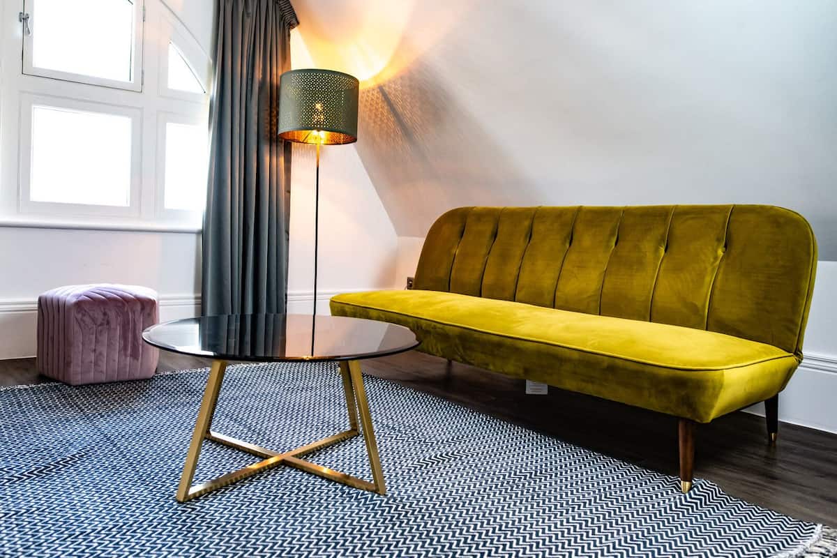 Una sala moderna con un sofá amarillo, una mesa redonda de cristal, una lámpara de pie y una alfombra estampada.