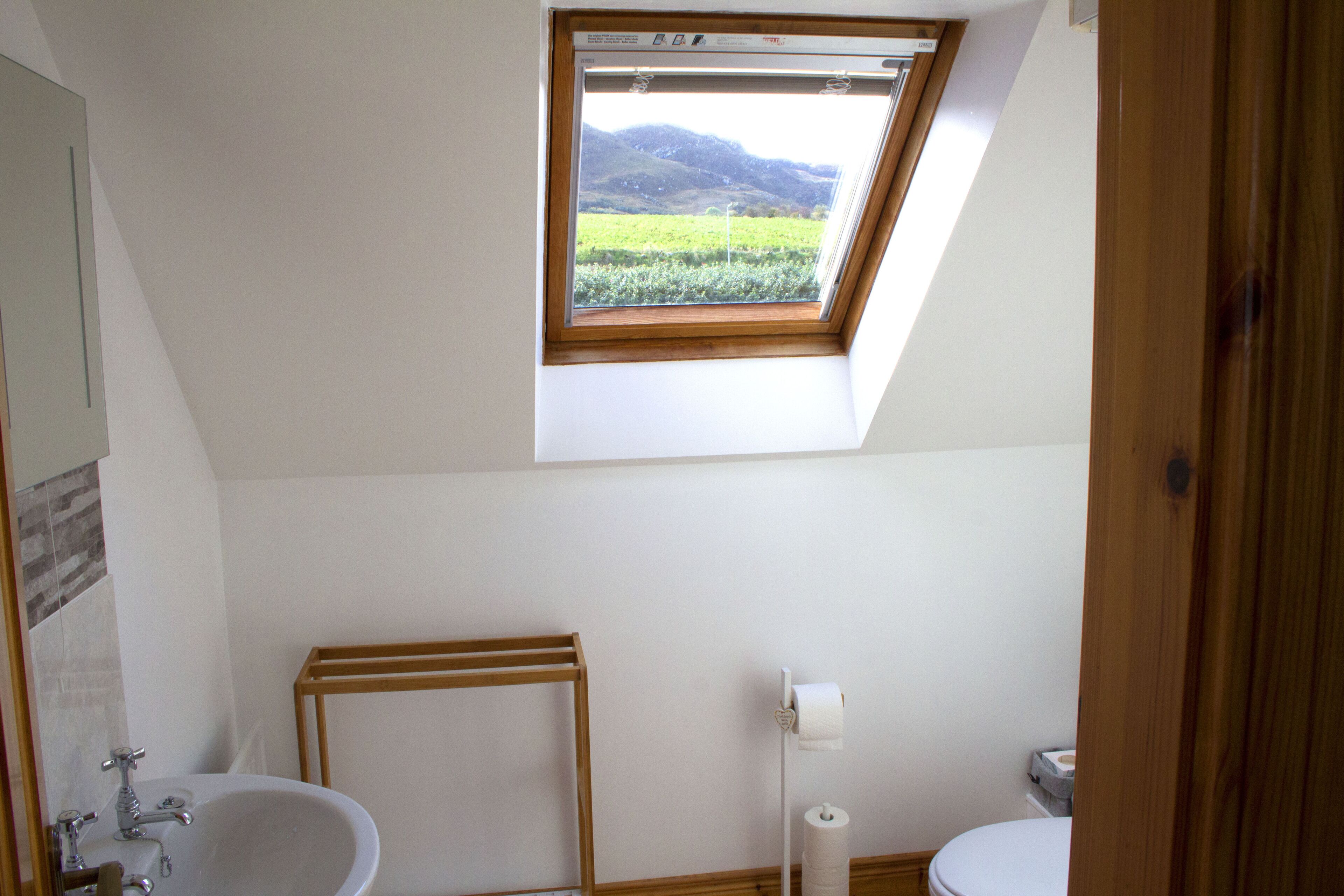 Un baño con tragaluz, bañera, inodoro y estante de madera.