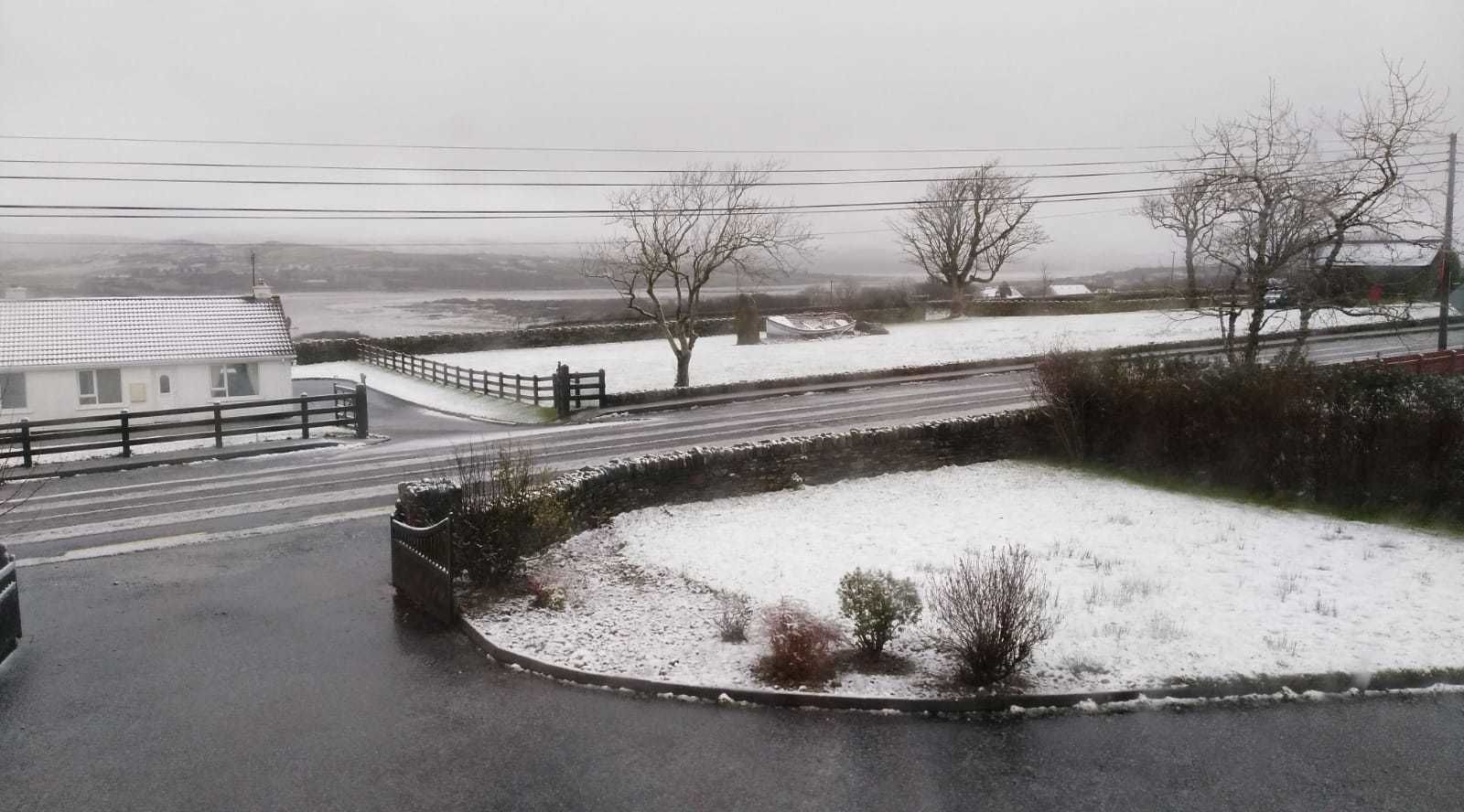 A rural road with a snow-covered landscape, a stone wall, and leafless trees.