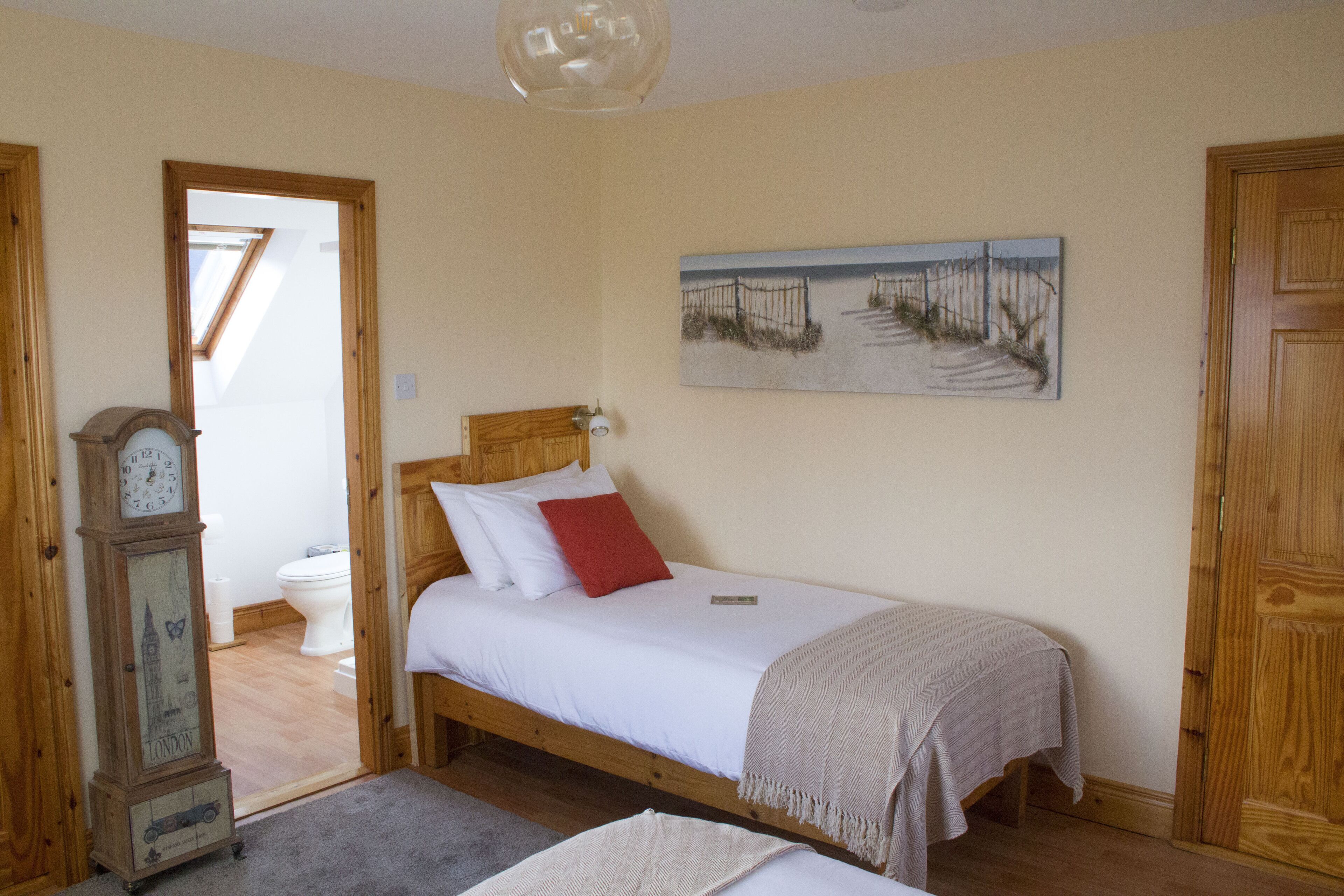 Un dormitorio con una cama, una puerta de madera, un cuadro y un reloj.