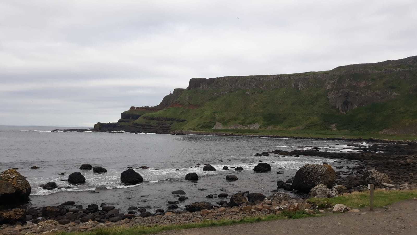 A coastal landscape with rocky shores, cliffs, and a grassy hill.