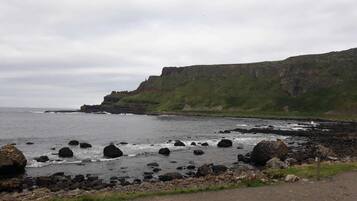 A coastal landscape with rocky shores, cliffs, and a grassy hill.