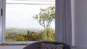 A room with a large window offering a view of a tree and rolling hills. - Madra Rua Organic Accommodation (Ballyliffin)