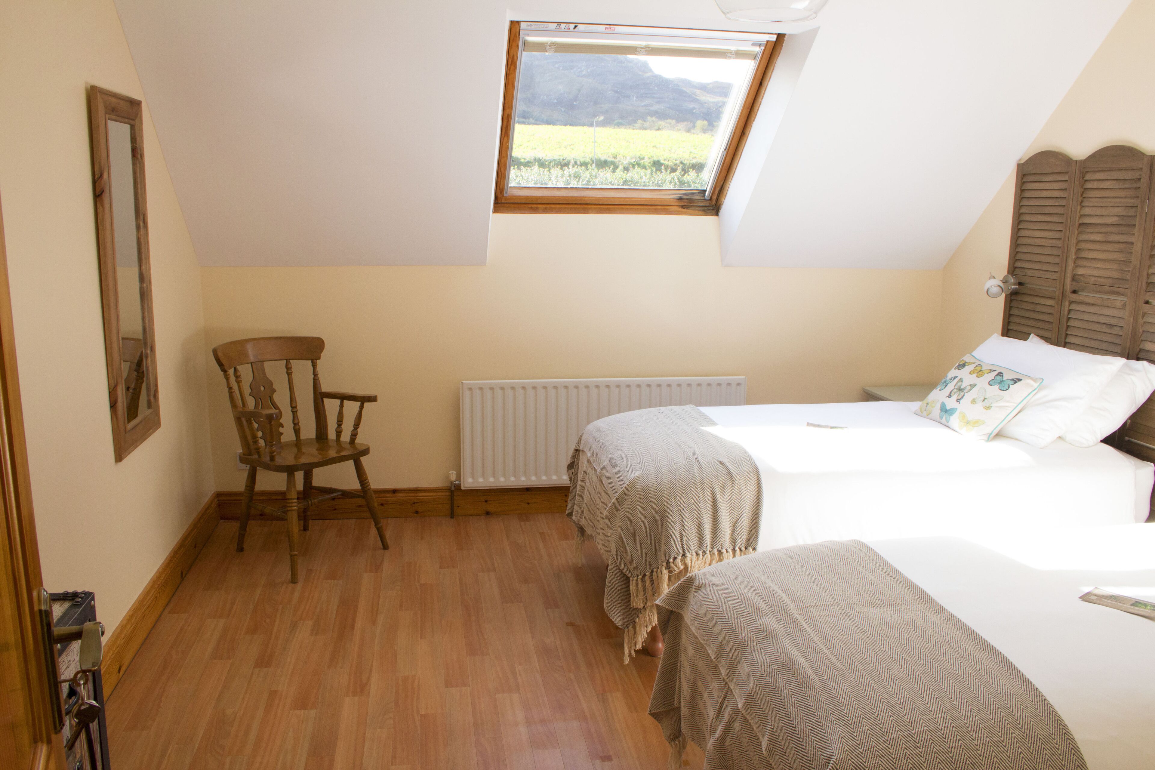 A bedroom with two beds, a wooden chair, a radiator, and a window with a view of the outdoors.
